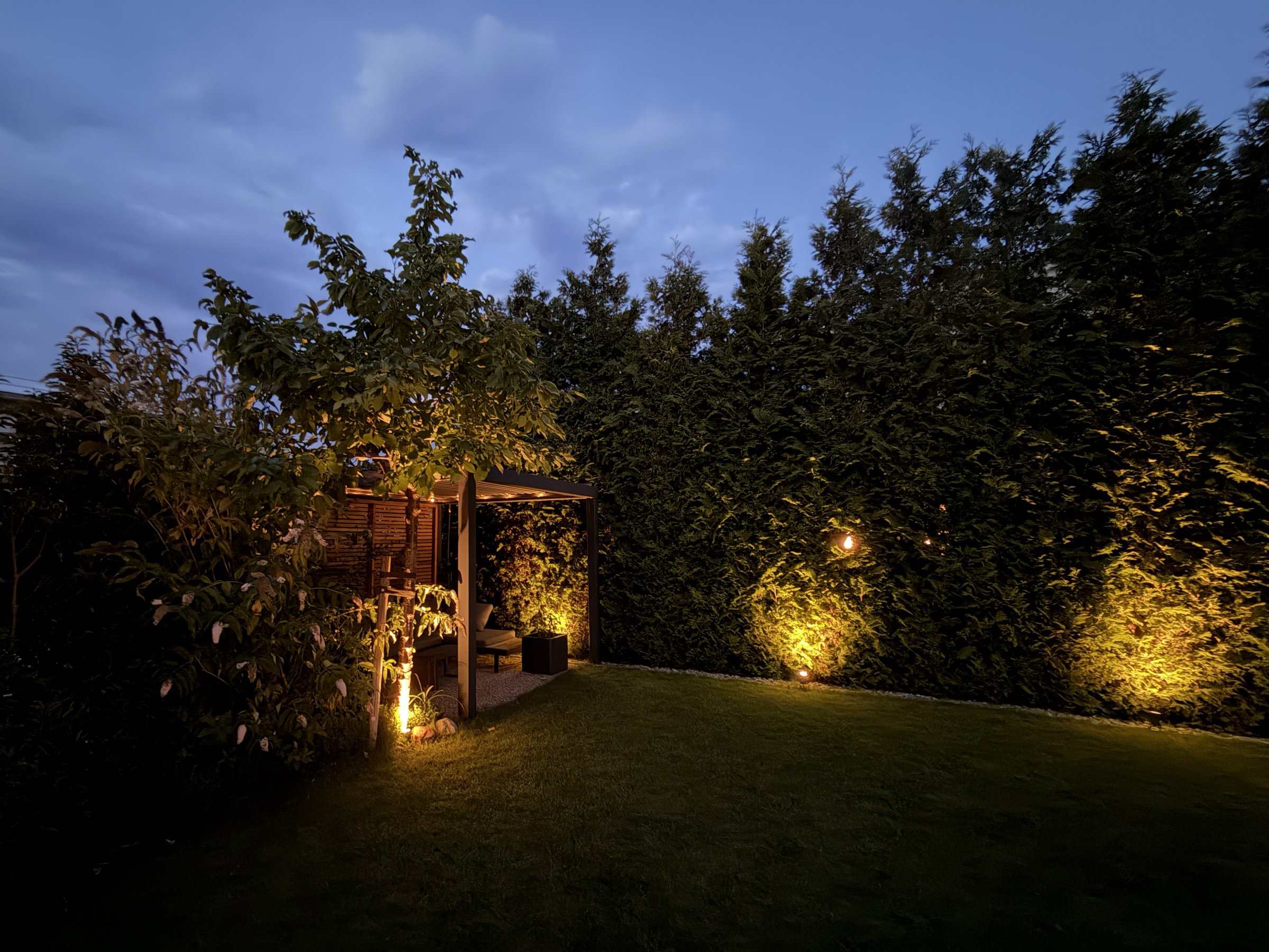 Pergola mit Gartenbeleuchtung in der Dämmerung